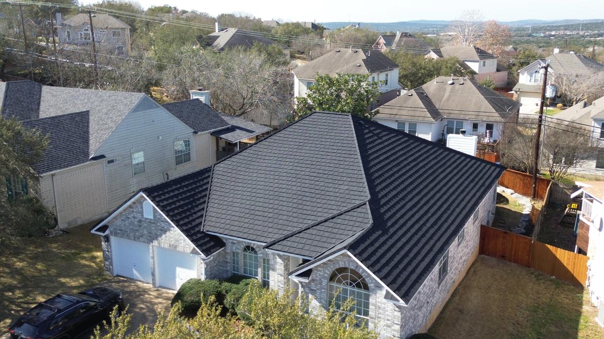 Drone view of a brick home with a charcoal roof in a hillside neighborhood