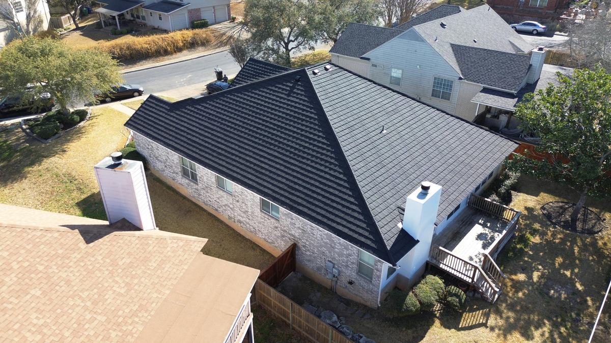Drone view of a brick home with a charcoal hip roof and a white chimney