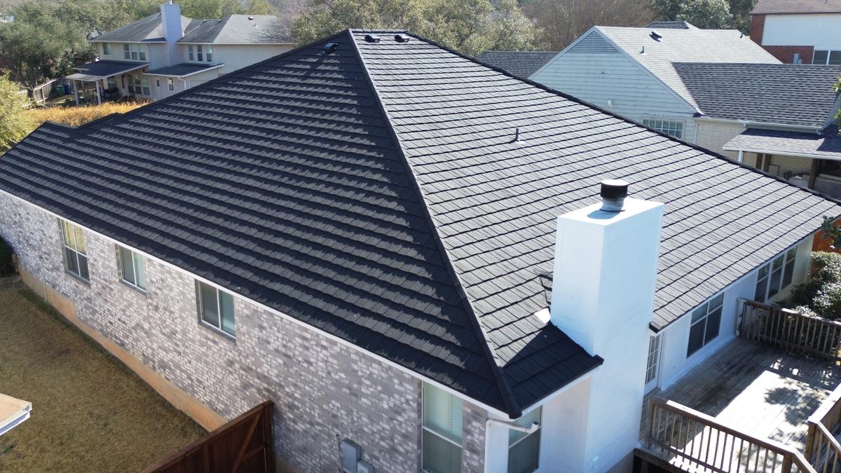 Drone view of a charcoal hip roof with a tall white chimney above a back deck